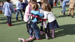 Petite fille atteinte d'arthrogrypose, dans une cours de maternelle, en motillo pour apprendre à marcher