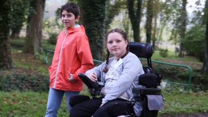 Fillette atteinte d'arthrogrypose, se promenant en fauteuil avec une amie.