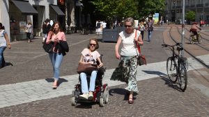 Jeune femme atteinte d'arthrogrypose, se déplaçant en fauteuil sur un trotoir